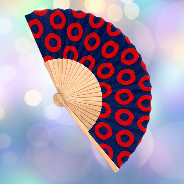 Handheld fan with red circular pattern on blue background against a blurred colorful background
