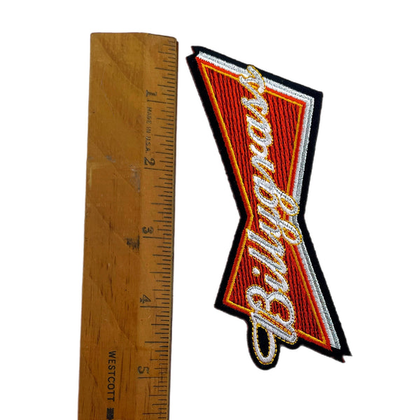 Patch of a well-known brand logo next to a wooden ruler for size reference on a white background