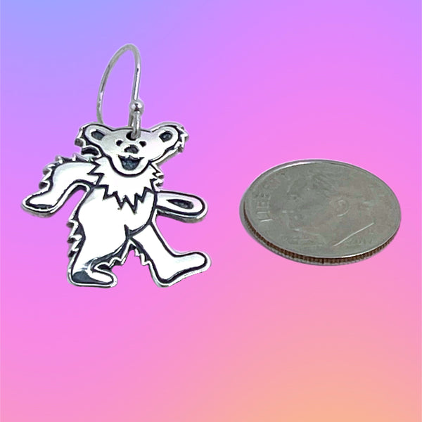 Silver bear-shaped earring next to a quarter on a gradient background