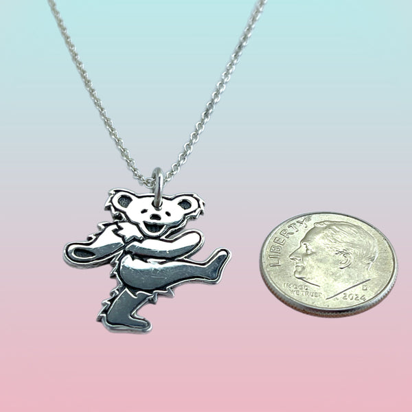 Silver pendant shaped like a bear on a chain next to a quarter for scale on a gradient background
